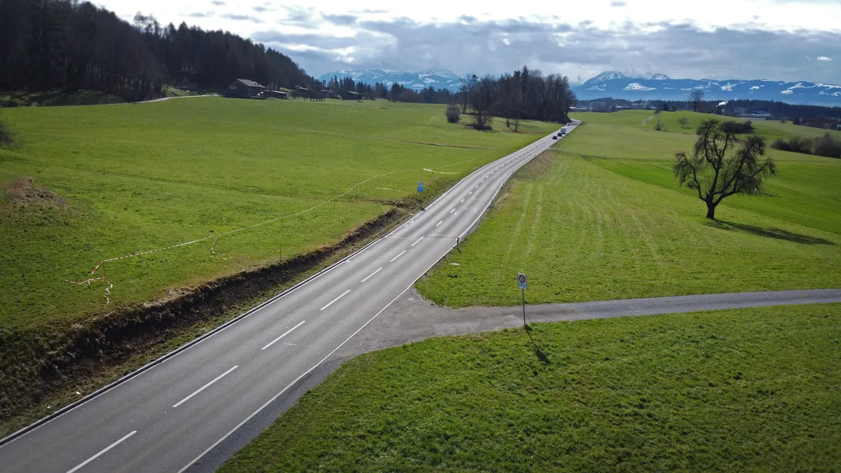 Eine Strasse, die durch Felder führt. Links sind Absperrbänder zu sehen. 